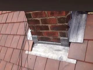Lead flashing fitted around a brick chimney on a tiled roof